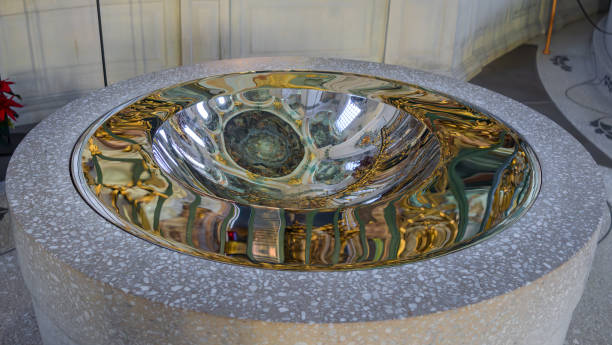 Sankt Gallen, Switzerland - January 1, 2025: A modern baptismal font with a reflective metallic basin set in a stone base in a cathedral of Sankt Gallen