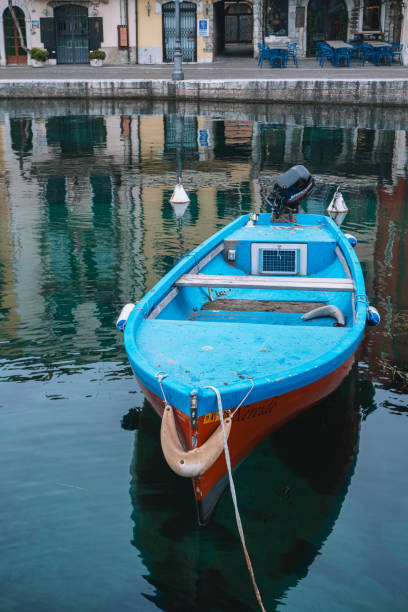 Lazise, Italy - 06.02.2024. Traditional wooden boats rest gently in the calm waters of the harbor, reflecting the peaceful and picturesque surroundings of the coastal town.
