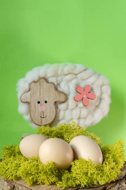 A charming wooden sheep decoration accompanied by Easter eggs on a textured green moss background. A warm and festive spring composition with natural elements.