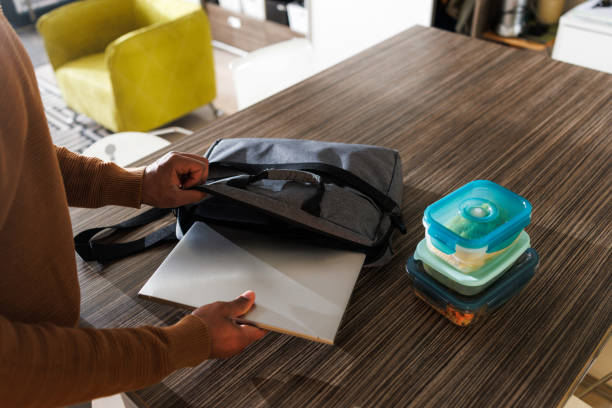 Person organizing daily items, packing lunch containers and a laptop, symbolizing preparation.