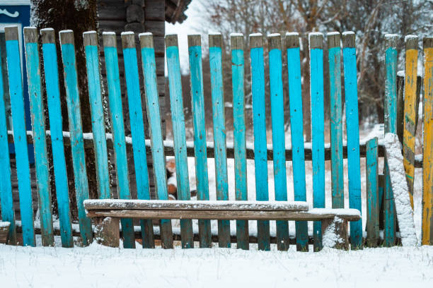 Blue wooden fence and bench on the street in Belarusian village in winter.