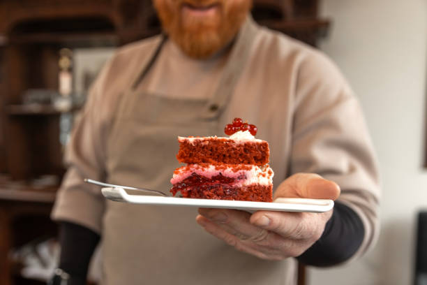 Stock photo of a luscious slice of red velvet cake, featuring rich, velvety layers beautifully complemented by smooth cream cheese icing and frosting. Its vibrant red hue makes it a stunning and colorful addition to any celebration