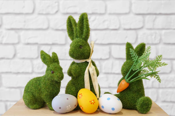istock Decorative green moss bunny figures with Easter eggs on wooden table on white brick wall background 2200361026