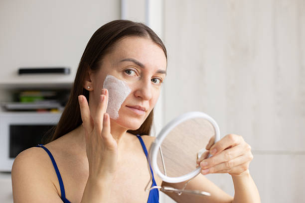 istock Smiling woman applying cream mask on her face. Cosmetics for problem skin. 2200362275