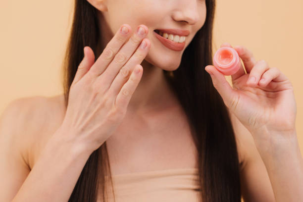 istock Woman applying lip balm on her perfect lips on beige background 2200364348