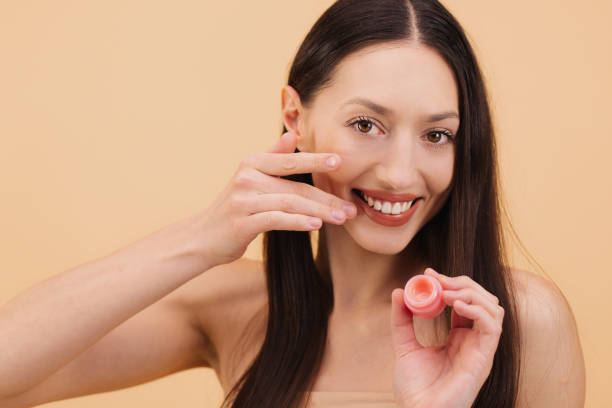 istock Smiling woman applying lip balm with finger on beige background 2200364376