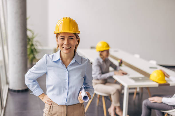 istock Female architect smiling and holding blueprints in office 2200369010