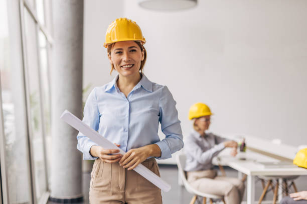 istock Female architect holding blueprints smiling at camera in office 2200369019