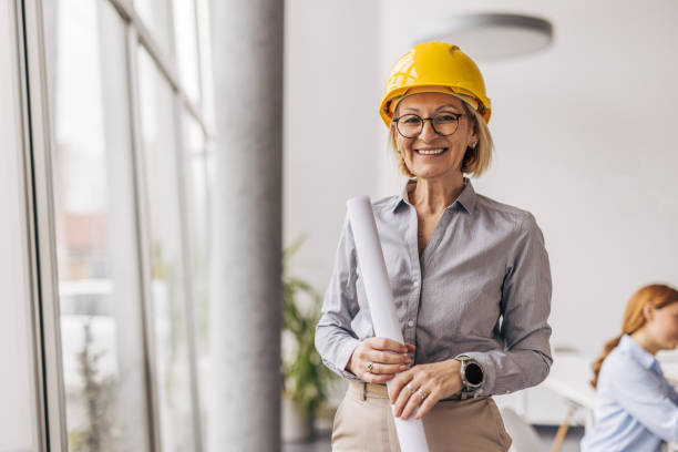 istock Senior female architect smiling and holding blueprints in office 2200369116