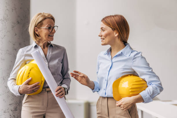 istock Female architects discussing blueprint plans wearing hardhats 2200369516