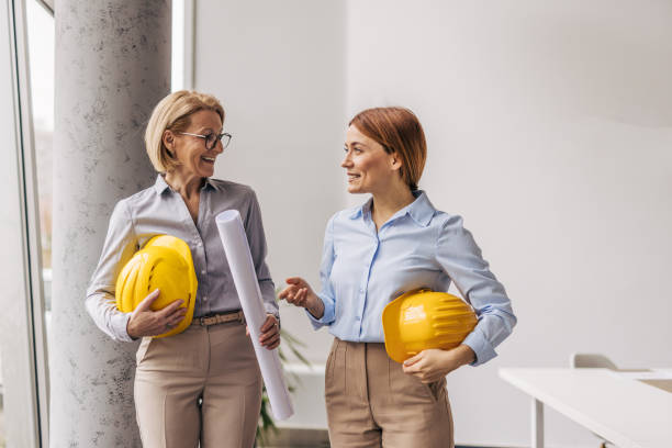 istock Two female engineers discussing a project holding blueprints and helmets 2200369517
