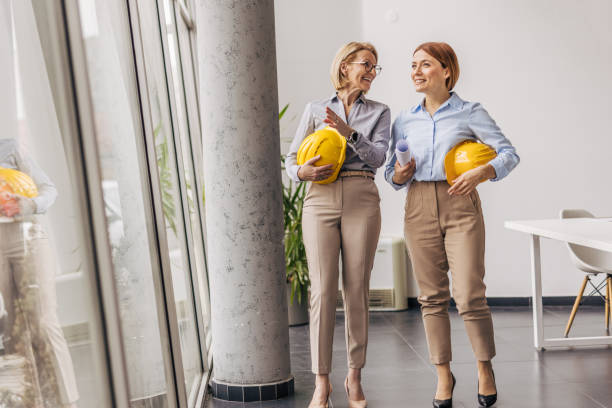 istock Female engineers walking and talking in office holding plans and hard hats 2200369617