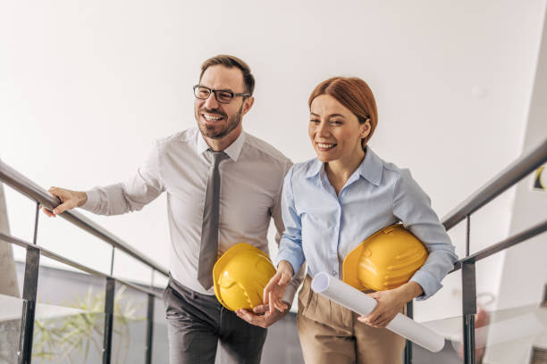 istock Smiling architects walking upstairs holding blueprints and hardhats 2200370098