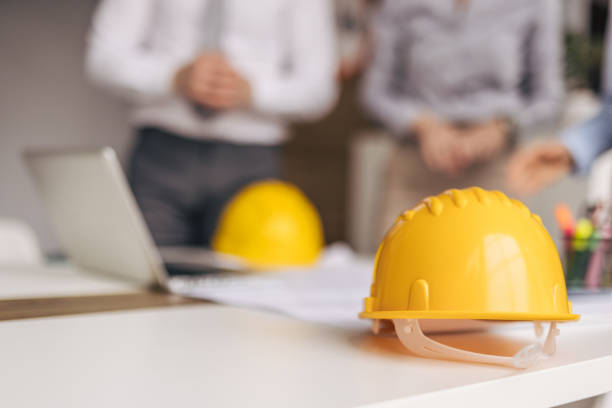 istock Yellow safety helmets sit on desk as architects discuss plans in background 2200370885
