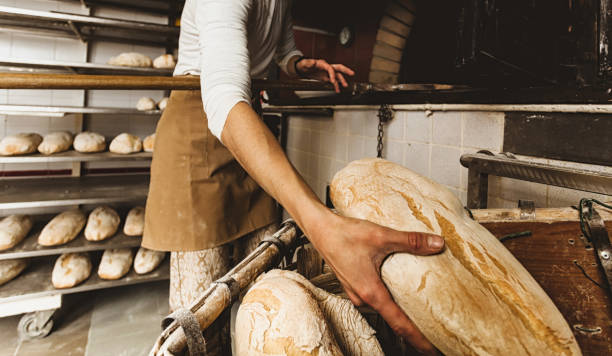 istock Baker taking fresh bread from a wooden container in a bakery 2200372846
