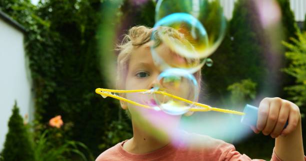 istock Curly-haired toddler releases even row of soap bubbles from plastic wand 2200375276