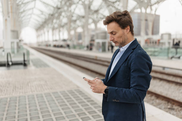 istock Man Standing With Phone In Quiet Train Station 2200376195
