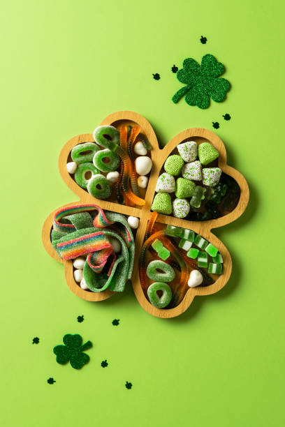 St. Patrick's Day candy tray with sweets and glitter shamrocks on green background. Flat lay, top view.