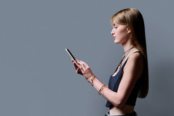 istock Fashionable young woman using smartphone, profile view, gray background 2200381312