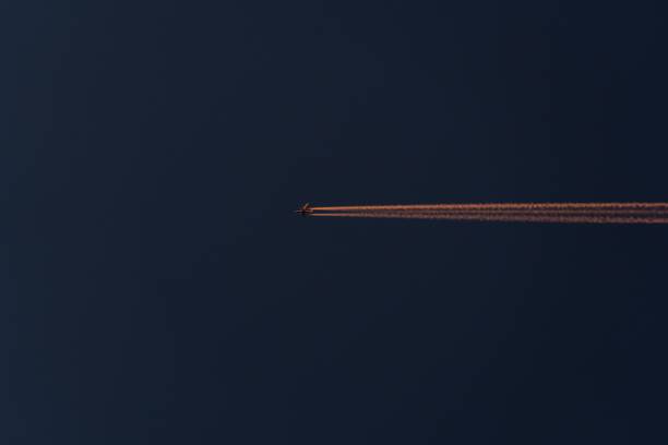 A high-altitude airplane leaves contrails against a dark sky at dusk, creating a visual contrast.