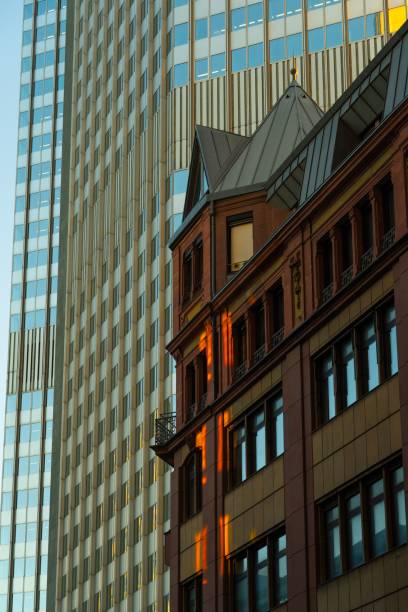 A modern skyscraper and historic building facade in downtown Frankfurt at sunset.