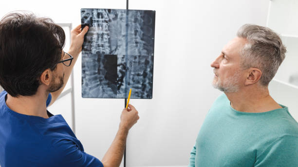 istock Manual therapist viewing X-ray of backbone with his mature male patient with spinal problem during medical consultation at hospital 2200384604