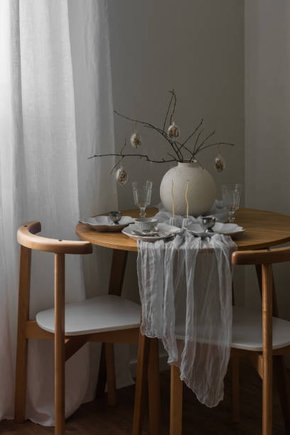 istock Festive Easter setting - Easter bouquet in a ceramic vase, dishes on a round wooden table in the living room 2200384999
