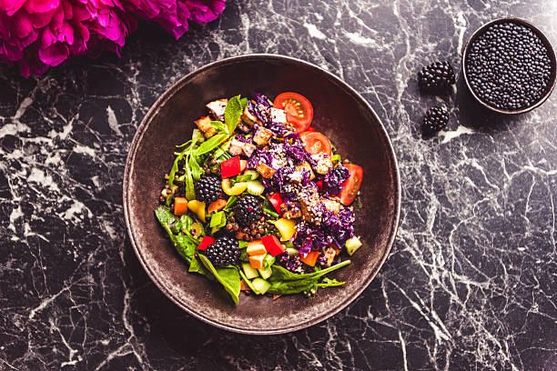 Fresh summer salad bowl with baby spinach, blackberries, tomatoes, red cabbage and avo - peonies in the background