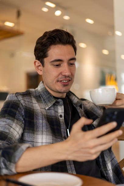 istock Young adult man drinking coffee and using mobile phone in a cafe 2200387634