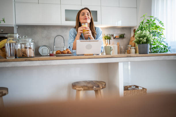 istock Woman enjoying breakfast and using tablet in modern kitchen 2200389261