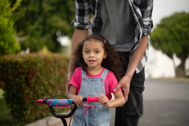 istock Road, teacher and helping child with bicycle, growth and development with cycling and neighbourhood. Outdoor, hands and travel with bike on street, kid and eco friendly transport for youth or people 2200389791