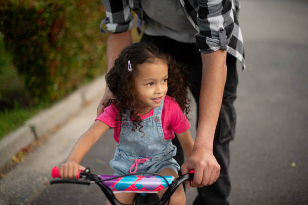 istock Girl, learning and helping child with bicycle, growth and development with cycling and neighbourhood. Outdoor, hands and travel with bike on street, family or eco friendly transport for kid or people 2200389798