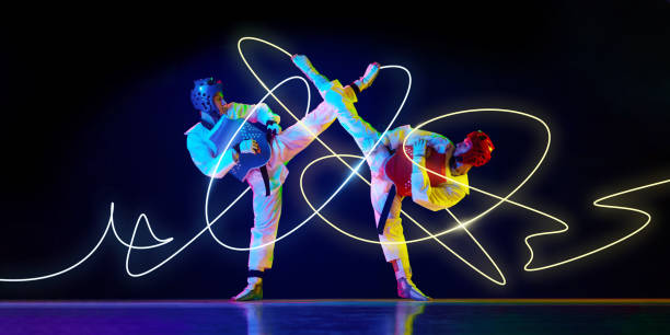 Two taekwondo fighters in synchronized high kicks, protective gear on, yellow neon trails swirling around movement, capturing power against black backdrop. Concept of sport, competition, tournament