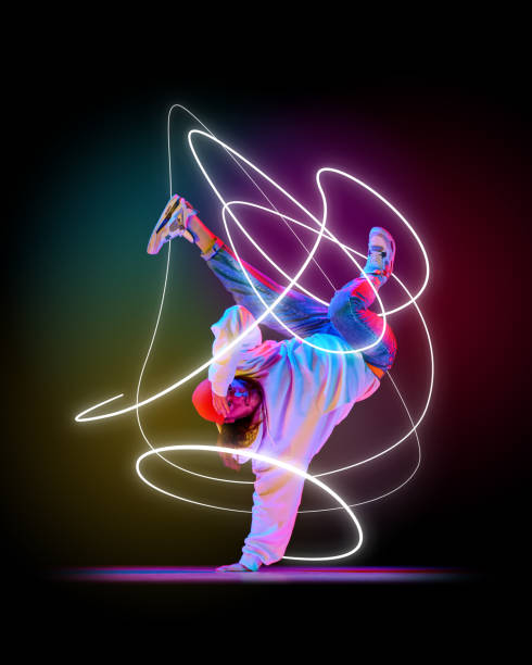 istock Male dancer, breakdancer balancing on one hand, with neon pink and white light swirls capturing rhythm against dark backdrop. 2200397591