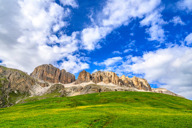 Sella group plateau-shaped massif in the Dolomites mountains  seen from the Passo Pordoi during a sprintime day in the Italian Alps. A footpath is winding through the Alpine meadow alms.