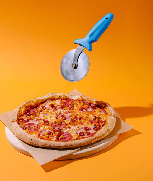 istock Pizza with vibrant orange background and a pizza cutter floating above ready for slicing 2200401733