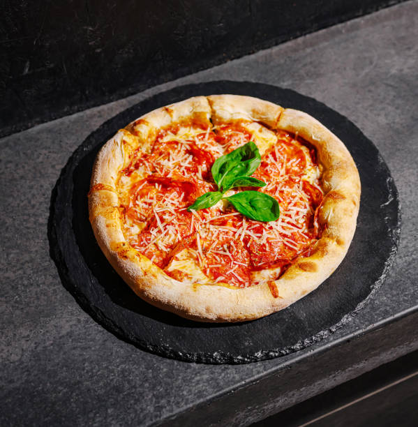 istock Classic margherita pizza with fresh basil on a dark stone surface in a warm kitchen setting topped with grated cheese 2200402065