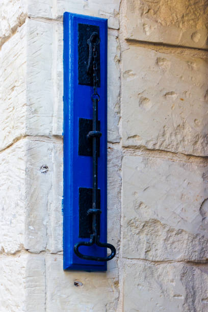 A close-up view of a blue and black metal doorbell switch mounted on a textured stone wall, showcasing vintage-style iron detailing and contrasting colors against a rustic urban exterior.