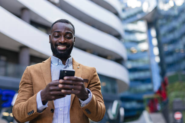 istock Smiling businessman using smartphone in front of modern office buildings 2200428368