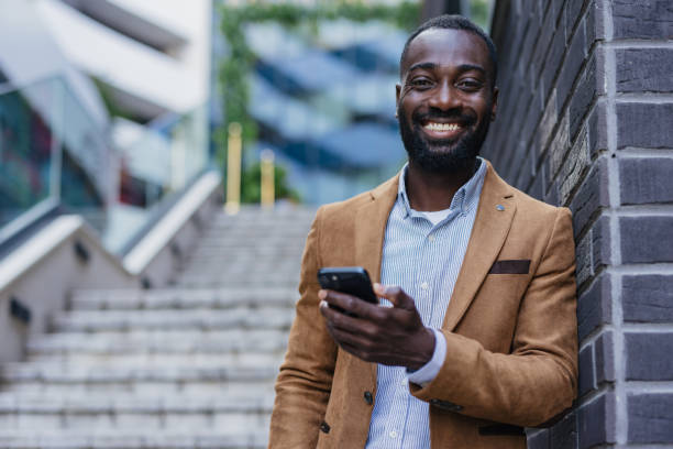 istock Smiling businessman using smartphone in front of modern building 2200428432