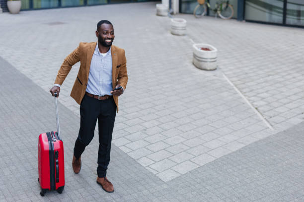 istock Smiling businessman walking with suitcase and using smartphone 2200428445