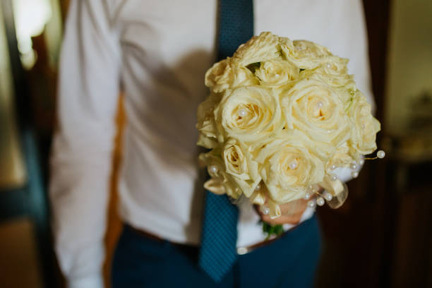 The groom is holding a beautiful bouquet of white roses.