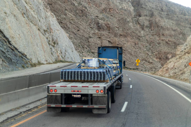 Truck navigating steep mountain road, surrounded by lush greenery, under clear blue sky.