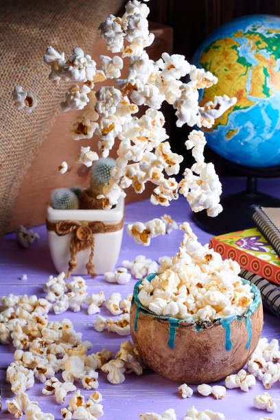 istock Popcorn falls into a bowl on table. Lifestyle with globe, cactus flower pot. Falling popcorn 2200433428