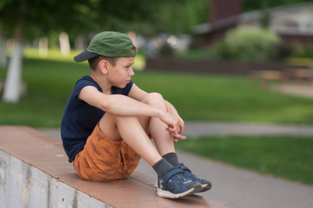 A teenage boy is squatting leaning against a concrete wall on the street. Upset and sad. Bullying. Quarrel with parents A teenage boy is squatting leaning against a concrete wall on the street. Upset and sad. Bullying. Quarrel with parents. sad teenager boy crying outdoors in park stock pictures, royalty-free photos & images