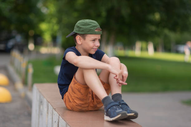 A teenage boy is squatting leaning against a concrete wall on the street. Upset and sad. Bullying. Quarrel with parents A teenage boy is squatting leaning against a concrete wall on the street. Upset and sad. Bullying. Quarrel with parents. sad teenager boy crying outdoors in park stock pictures, royalty-free photos & images