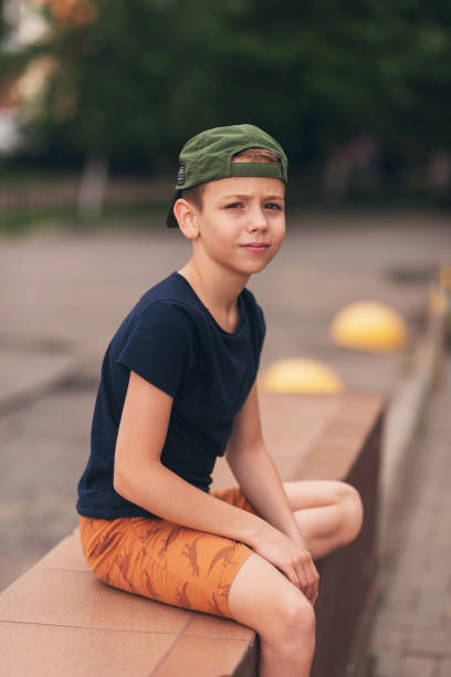 A teenage boy is squatting leaning against a concrete wall on the street. Upset and sad. Bullying. Quarrel with parents A teenage boy is squatting leaning against a concrete wall on the street. Upset and sad. Bullying. Quarrel with parents. sad teenager boy crying outdoors in park stock pictures, royalty-free photos & images