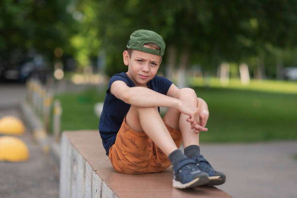 A teenage boy is squatting leaning against a concrete wall on the street. Upset and sad. Bullying. Quarrel with parents A teenage boy is squatting leaning against a concrete wall on the street. Upset and sad. Bullying. Quarrel with parents. sad teenager boy crying outdoors in park stock pictures, royalty-free photos & images
