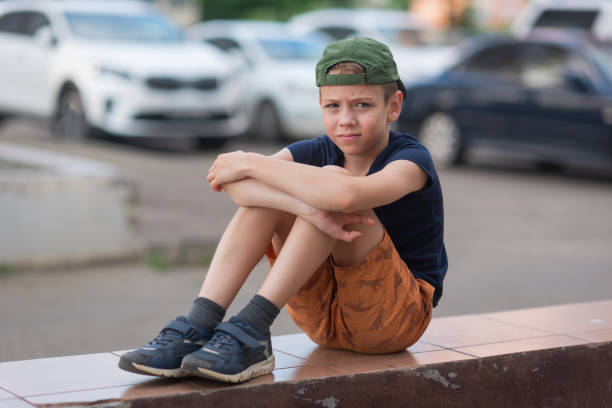 A teenage boy is squatting leaning against a concrete wall on the street. Upset and sad. Bullying. Quarrel with parents A teenage boy is squatting leaning against a concrete wall on the street. Upset and sad. Bullying. Quarrel with parents. sad teenager boy crying outdoors in park stock pictures, royalty-free photos & images