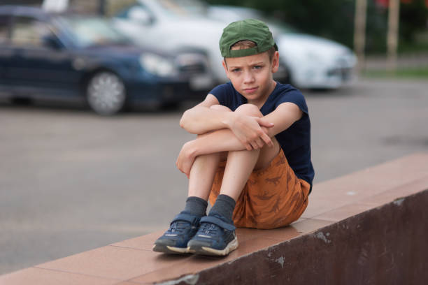 A teenage boy is squatting leaning against a concrete wall on the street. Upset and sad. Bullying. Quarrel with parents A teenage boy is squatting leaning against a concrete wall on the street. Upset and sad. Bullying. Quarrel with parents. sad teenager boy crying outdoors in park stock pictures, royalty-free photos & images